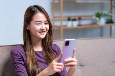 Kanepede oturmuş, canlı bir sohbetin içinde akıllı telefonuyla konuşan genç bir kadın videosu..