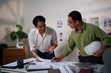 Mühendisler, toplantı masasında proje hesaplamaları, planlar, dizüstü bilgisayarlar ve teknik araçlar kullanarak birlikte çalışıyorlar..