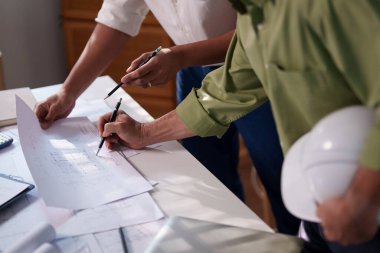 Mühendisler, toplantı masasında proje hesaplamaları, planlar, dizüstü bilgisayarlar ve teknik araçlar kullanarak birlikte çalışıyorlar..