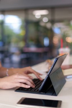 Genç Asyalı kadın, modern bir üniversite kafesinde tabletle ders çalışıyor.