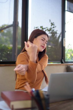 İş kadını elinde laptop ve belgelerle doğal temalı bir ofiste esniyor. Ahşap bir masada işe ara veriyor..