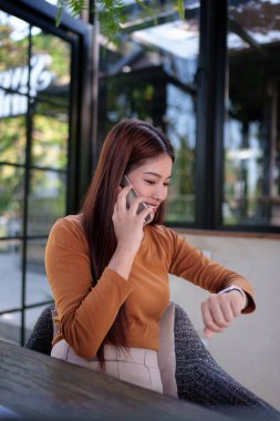 İş kadını, telefonda konuşurken akıllı saati kontrol ediyor. Hem de doğal temalı bir ofiste. Çoklu görev ve meşgul..