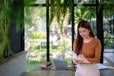 İş kadını, profesyonel verimlilik için planlama ve organizasyona odaklanan doğal temalı bir ofiste notlar alıyor.