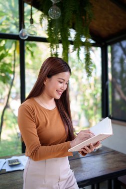 İş kadını, profesyonel verimlilik için planlama ve organizasyona odaklanan doğal temalı bir ofiste notlar alıyor.