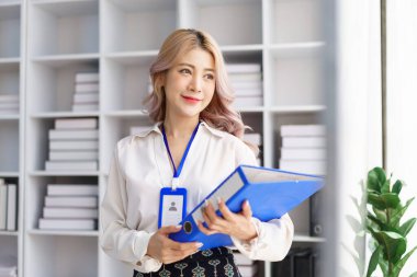 Düzenli çalışma alanındaki belgeleri yönetirken elinde birden fazla dizin tutan akıllı ofis kadını