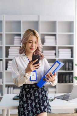 Modern çalışma plağında dizinleri ve çoklu görevleri yönetirken telefonu kontrol eden akıllı iş kadını