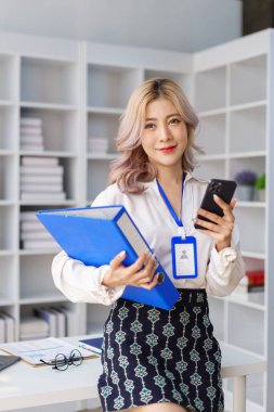 Modern çalışma plağında dizinleri ve çoklu görevleri yönetirken telefonu kontrol eden akıllı iş kadını