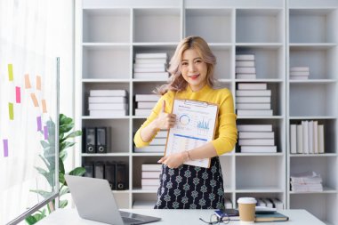 Kendine güvenen iş kadını, parlak modern ofiste iş raporu klasörünü tutarken başparmak kaldırıyor.