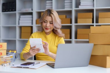 Genç bayan girişimci dijital tablette ürün maliyetini hesaplarken evde online mağaza envanterini yönetiyor