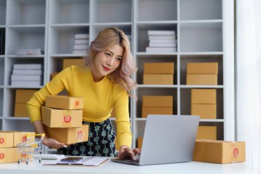 Çevrimiçi işletme sahibi ev ofisteki dizüstü bilgisayarda çalışırken müşteri siparişlerini ve kutuları yönetiyor.