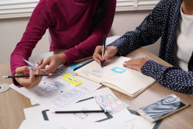 İki yetişkin Asyalı kadın kullanıcı arayüzü tasarımında işbirliği yapıyor. Fikirleri beyin fırtınası yaparlar, kablolar çizerler, ve mobil uygulamalar için kullanıcı deneyimini rafine ederler, tasarım düşüncesini teşvik ederler..