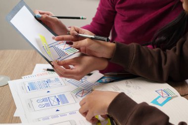 UI UX tasarım ekibinde çalışan yetişkin Asyalı kadınlar, tasarım taslakları ve kalemlerle mobil uygulama kullanıcı arayüzü çiziyorlar. İlgili tasarım için beyin fırtınası iş akışı.