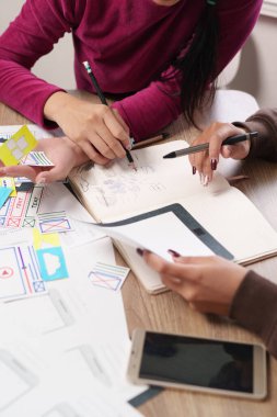 Yetişkin Asyalı kadın tasarımcılar mobil uygulama ve web sitesi kablosuz bağlantıları, beyin fırtınası kullanıcı deneyimi ve proje iş akışı planlaması için UI UX tasarım taslakları üzerinde işbirliği yapmaktadırlar..