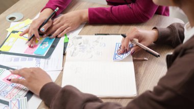 İki yetişkin Asyalı tasarımcı bir UI tasarım projesinde işbirliği yapıyor. Yeni arayüz kavramsallaştırması için eskizler ve kağıt modellemeleri içeren beyin fırtınası mobil uygulama düzeni.