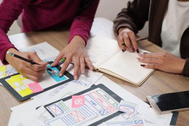 Asyalı kadın UI tasarımcıları ekibi internet sitesi ve mobil uygulama arayüzü tasarımı üzerinde çalışıyor, kullanıcı dostu deneyimler ilk stratejisini oluşturmak için birlikte beyin fırtınası yapıyorlar.