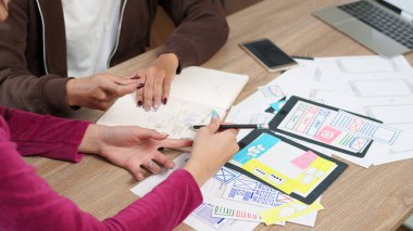 İki yetişkin kadın, mobil uygulama için kullanıcı arayüzü, beyin fırtınası ve çizim fikirleri üzerinde işbirliği yapıyor. Bu resim yinelemeli tasarım sürecini eylem sırasında yakalar.