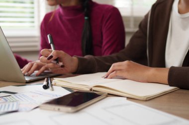 Asyalı kadın UI UX tasarımcıları arayüz tasarımı üzerinde birlikte çalışıyorlar. Dizüstü bilgisayar, defter ve çizimler kullanarak beyin fırtınası yapmak. Kusursuz bir uygulama için kullanıcı deneyimi geliştiriliyor