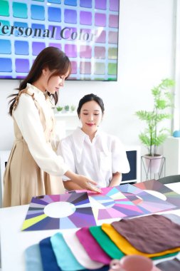 Asyalı kadın müşteriyle kişisel renk analizi. Stilist mükemmel renk paletini bulmaya yardım ediyor. En iyi stil ve güzellik sezonunuzu bizim rehberliğimizle keşfedin..