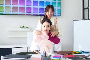 Asyalı genç kadınlar kişisel renk analizinden geçiyor, kumaş seçiyorlar. Kişisel stilistle danışma, müşterilerin ten rengi paleti ve giysi dolabını tanımlamalarına yardımcı olur.