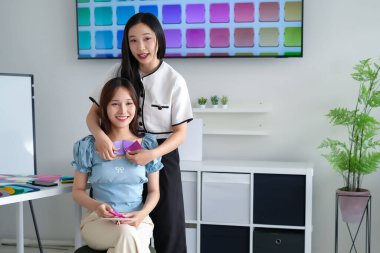 Kişisel renk danışmanlığı sırasında iki genç Asyalı kadın. Bir stilist, müşteriye kıyafet makyajı için en iyi renkleri seçmesinde yardımcı olur. Derinin alt tonlarına odaklan Renk paleti eşleşmesi.