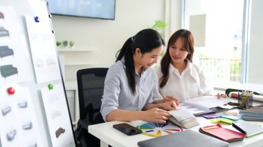 İki yetişkin Asyalı kadın iç mimar kumaş rengi paletinde işbirliği yapıyorlar. Ev dekorasyonu için tasarım fikirleri tartışıyoruz. İç tasarım konsepti, kumaş örnekleri ve renk çarkı.