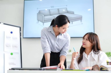 İki genç Asyalı iç mimar parlak, modern bir ofiste bir kanepe tasarımı projesinde işbirliği yapıyorlar. Mobilya çizimlerine, örnek çizimlerine ve galeri alanındaki işbirliğine bakın.