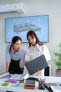 Kanepe tasarımı ve renk şeması üzerinde çalışan iki genç Asyalı kadın iç mimar. Renk örnekleri, kumaş örnekleri ve dizüstü bilgisayarla modern ev yenileme fikirlerini tartışıyorlar. Uzay planlamasına ve malzeme seçimlerine odaklan.