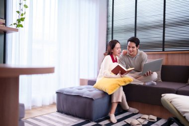 Asyalı yetişkin bir çift oturma odasında dinleniyor. Adam dizüstü bilgisayar kullanırken kadın bir kitap okuyor. Modern bir evde boş zamanlarının tadını çıkarıyorlar..