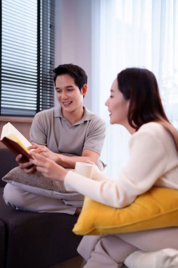 Evde birlikte kitap okuyan Asyalı bir çiftin sıcak bir anını yakalıyorum. Sıcak atmosferin ve rahatlığın tadını çıkar. Ev yaşam tarzı içeriği için ideal.