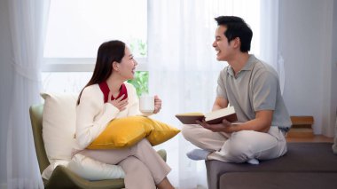 Birlikte olmanın özünü, Asyalı yetişkin bir çiftin evde rahat vakit geçirdiği görüntüsüyle yakalayın. Asyalı adam kitap okurken Asyalı kadın elinde bir fincan kahve tutuyor..