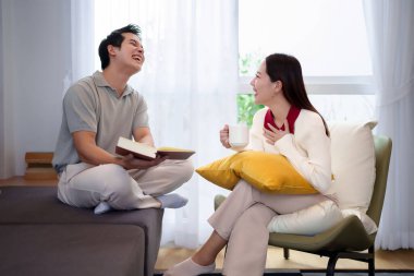 Asyalı neşeli bir çiftin sıcak bir oturma odasında, elinde kahve fincanı tutan Asyalı kadın kitabı okuyan yumuşak, hafif Asyalı bir adamın birlikte gülüşü ılık bir atmosfer yaratıyor..