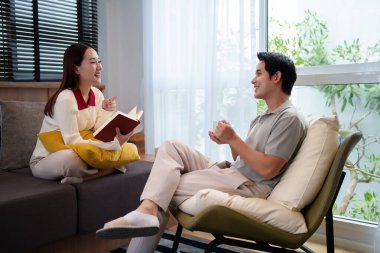 Ev rahatlığının özünü, modern oturma odalarında birlikte kahve içip kitap okuyan Asyalı genç bir çiftin görüntüsüyle yakalayın..