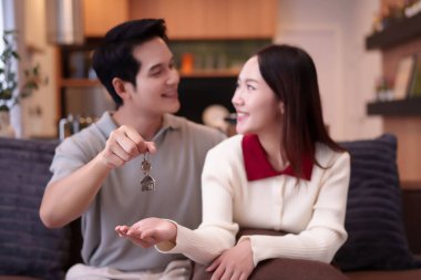 Yetişkin bir Asyalı çift yeni evlerinin anahtarlarını tutarken gülümsüyor, hayallerindeki evi kutluyorlar, ipotek onayı, gayrimenkul yatırımı, emlak alımı ve konut başarısı..