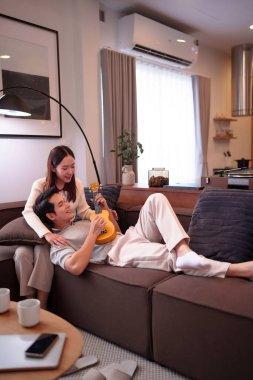 Asyalı bir çiftin oturma odasında dinlenirken sakin bir anını yakalayan erkek gitar çalarken kadın onu modern oturma odası Love Bergetherness 'i seyrediyor.