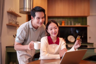 Mutlu bir Asyalı çift, yetişkin bir kadın ve erkek, evlerinde laptop ve kredi kartıyla online alışveriş yaparken gülümsüyor. Rahatlamak, rahatlıkla satın almak ve birlikte zaman geçirmek..
