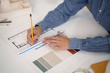 Yaşlı bir Asyalı el, ölçekli cetvelle bir plan çizerken görülüyor. El dikkatlice bir tasarım planı çiziyor. El, tasarım sergisi mimari el, ayrıntılı planları çiziyor..