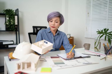Yaşlı Asyalı kadın mimar, müşteri projeleri için ev tasarımı modeli tasarlıyor. İnşaat işindeki Asyalı kadın, iş yeri inşaatında mimarla ev tasarımı planını gözden geçiriyor..