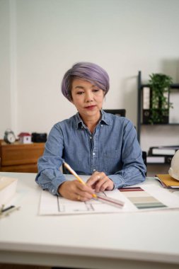 Asyalı bir kadın mimarın iç tasarım projesinin planlarını çizdiği bu büyüleyici görüntüyü keşfedin Asyalı kadın mimar ofisinde titizlikle mimari planları hazırlıyor..