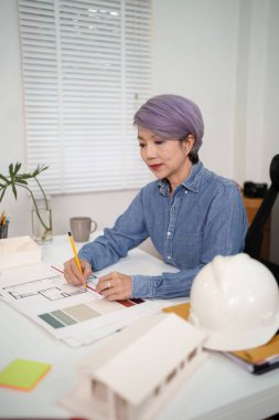 Asyalı yaşlı bir mimar, ev inşaatı için dikkatlice bir tasarım hazırlıyor. Profesyonel mimar, Desk İnşaat Projesi 'ni tasarlıyor..