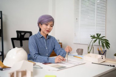Asyalı bir kadın mimar bina planı tasarlıyor. Eski bir profesyonel mimari tasarımcısı iş yerinde mimari tasarım planı hazırlar. Tasarımında doğruluğu sağlamak için bir pusula kullanarak hassasiyete odaklanmış.