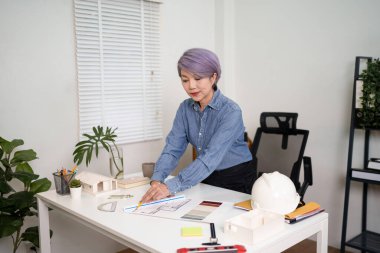 Ev tasarımı projesi için masa başında çalışan Asyalı yaşlı kadın mimar ev tasarımı mimarisi tasarlıyor. Mükemmel ev için detaylara odaklan..