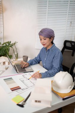 Asyalı kadın mimar, inşaat ofisi için dizüstü bilgisayar ve kalem kullanarak mimari tasarım fikirleri ve tasarım üzerinde çalışıyor. Dijital araçlarla mimari tasarım.
