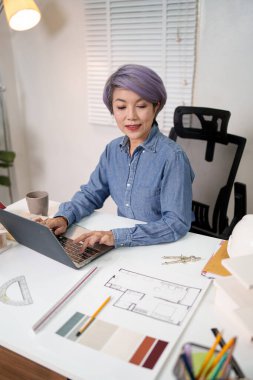 Yeni bir ev tasarlamak için dizüstü bilgisayarda çalışan yaşlı Asyalı kadın mimar. Eski profesyonel mimar ev planlarını gözden geçiriyor. Mimar masasında dizüstü bilgisayarında ev tasarımı ve tasarımı yapıyor..