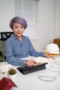 Asyalı mimar bir bina tasarımı projesi planlıyor Asyalı kadın yeni inşaat projesi için tablet kullanarak planları analiz ediyor Asyalı kadın inşaat fikri için dijital aletler kullanıyor