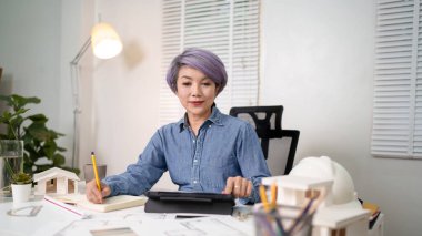 Yaşlı Asyalı kadın, bir sonraki ev projesini Asya kadınının planlarını titizlikle analiz ediyor. Yenilikçi ve pratik ev inşaatı konusunda sarsılmaz bir odak noktası olduğunu gösteriyor. Yaşlı Asyalı kadın kendini ev tasarımlarına adamıştır.