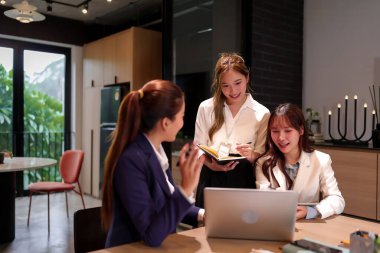 Üç Asyalı kadın modern ofis ortamında bir projede işbirliği yapıyorlar. İş görüşmeleri için dizüstü bilgisayar ve defter kullanırken yeni fikirleri ve beyin fırtınalarını tartışan bir takım olarak çalışıyorlar..