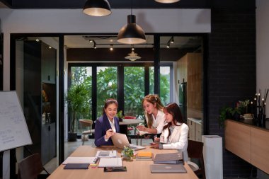 Modern bir ofiste strateji ve takım çalışmasını tartışan üç genç Asyalı kadın bir iş planı üzerinde çalışıyor. Profesyonel bir toplantıda verileri analiz ederek başlangıç başarısı üzerinde birlikte çalışmak.