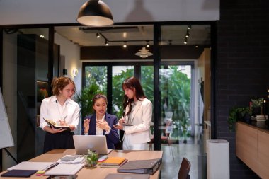 Modern ofis alanındaki bir toplantıda bir projede işbirliği yapan üç Asyalı kadın, başarı için profesyonel bir ortamda iş stratejisi ve takım çalışmasını tartışıyor..