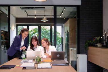 Üç Asyalı kadın modern bir ofis alanında bir projede işbirliği yapıyorlar. Bir dizüstü bilgisayardaki verileri analiz ediyorlar. İş görüşmesi yapıyorlar. Proje stratejisini tartışıyorlar.