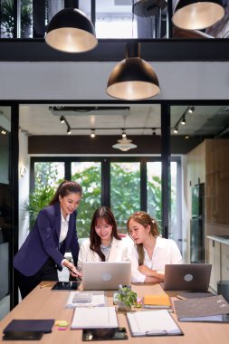 Üç Asyalı kadın, modern bir ofis alanında dizüstü bilgisayarda iş birliği yapıyor bir toplantı sırasında proje fikirlerini tartışıyorlar takım çalışması ve beyin fırtınası oturumu proje planlaması için gereklidir